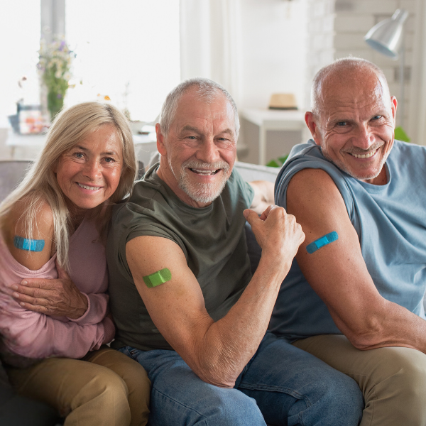 Three people sitting on couch showing off their vaccine Band Aids